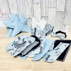 May include: A set of blue and gray fabric pieces with a cartoon character print. The set includes a crown, a bow tie, and two stars. The fabric pieces are all edged with a zig-zag stitch.