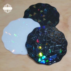 May include: Three round coasters with a mosaic design. The coasters are black with iridescent glitter embedded in the resin. One coaster is white with iridescent glitter.