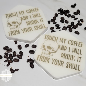 May include: Two white hexagonal coasters with a gold skull and the text "TOUCH MY COFFEE AND I WILL DRINK IT FROM YOUR SKULL".