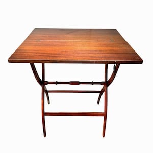 May include: A vintage, square, wooden table with a rich, reddish-brown finish. The table features a folding design with curved legs and a decorative horizontal support. The tabletop measures approximately 30 inches square.