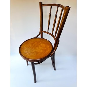 May include: A wooden chair with a dark brown finish and a circular seat. The seat features a light brown wood grain surface with a subtle floral inlay pattern. The backrest consists of a curved top rail supported by four vertical spindles.