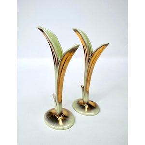 May include: A pair of ceramic bud vases featuring a tall, slender, leaf-like silhouette. Each vase has a pale mint green interior and exterior finish, accented with a metallic gold luster glaze along the outer edges and the circular base.