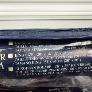 Op de afbeelding: Een marineblauwe kussensloopverpakking met maatdetails gedrukt op een donkerblauw label. Het label vermeldt standaard, king en European Square maten, met afmetingen in inches en centimeters.