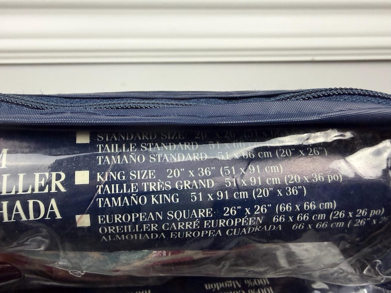 Op de afbeelding: Een marineblauwe kussensloopverpakking met maatdetails gedrukt op een donkerblauw label. Het label vermeldt standaard, king en European Square maten, met afmetingen in inches en centimeters.