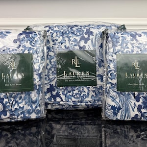 May include: Three packages of bedding sets with a blue and white floral pattern. Each package has a green label with the brand name "LAUREN" and the text "One King Sham". The bedding sets are in clear plastic packaging.