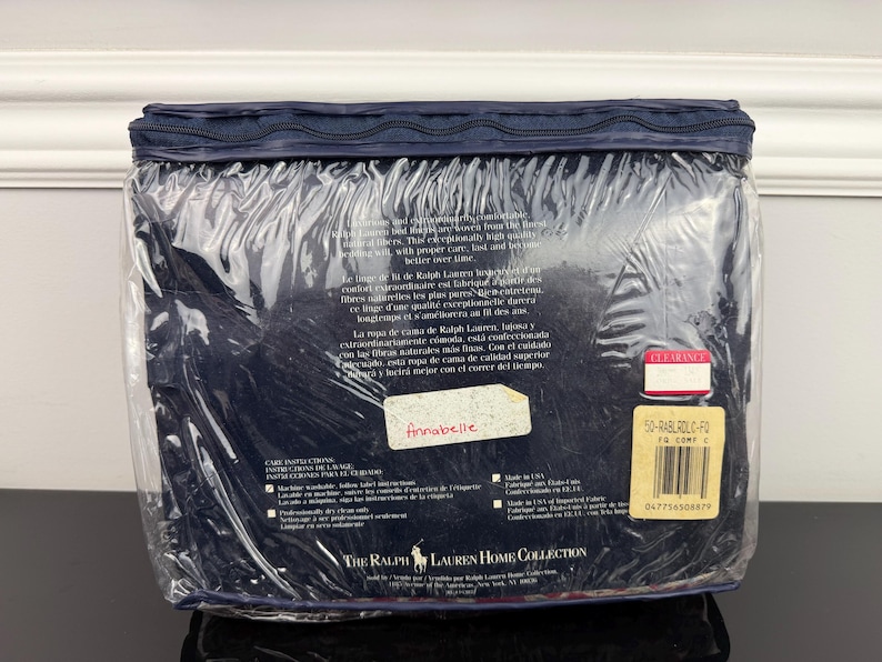 Op de afbeelding: Een marineblauwe beddengoedset, verpakt in doorzichtig plastic. De verpakking bevat tekst in meerdere talen, een "Clearance"-sticker en een label met een streepjescode. De set is van The Ralph Lauren Home Collection.