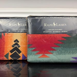 May include: Two packaged Ralph Lauren king flat sheets. The packaging is black with the brand logo and text. The sheets have colorful geometric patterns in shades of orange, red, green, and purple. The sheets are 108 x 102 inches.