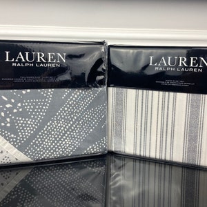 May include: Two packaged sets of Lauren Ralph Lauren bedding. One set features a gray and white geometric pattern, the other a white and gray striped pattern.