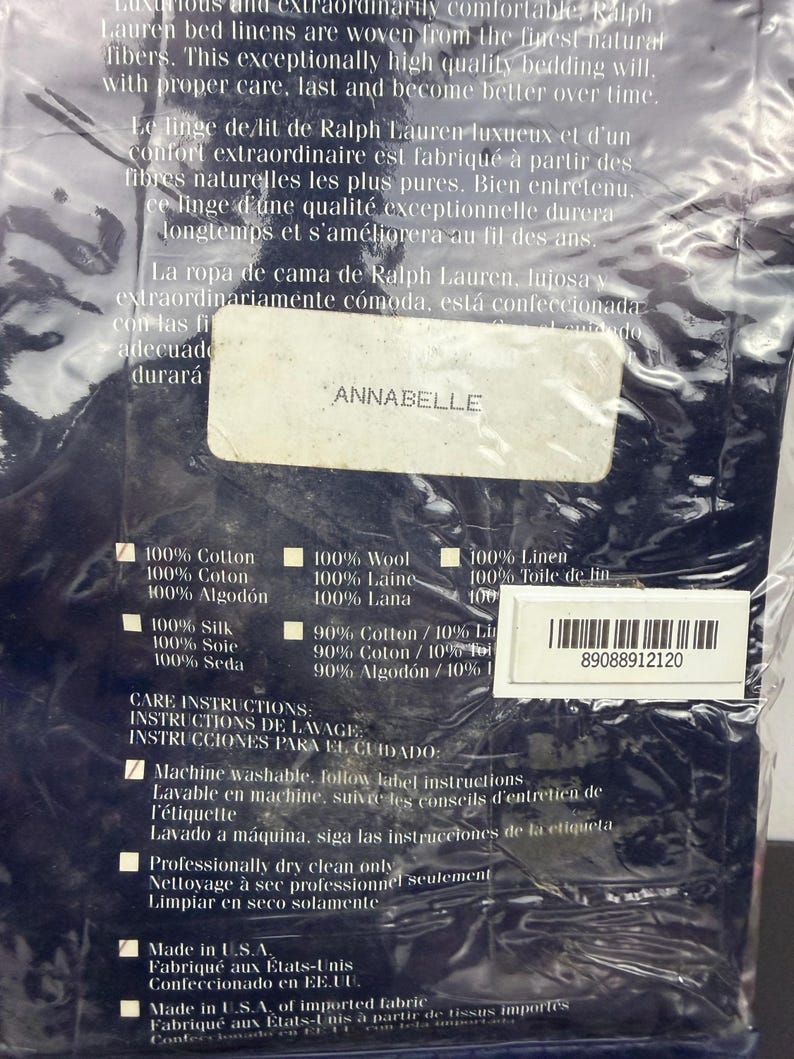 Op de afbeelding: Een verpakking van Ralph Lauren beddengoed. Het label luidt "ANNABELLE" en vermeldt de samenstelling van de stof, waaronder 100% katoen en linnen. Er worden ook onderhoudsinstructies gegeven, waaronder machinewas en professionele chemische reiniging.