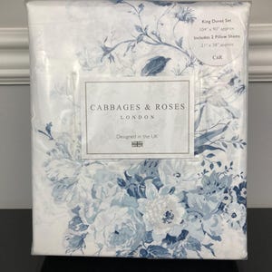 May include: A King duvet set in a clear plastic package. The bedding features a floral pattern in shades of blue and white. The package includes two pillow shams. The text "CABBAGES & ROSES LONDON" and "Designed in the UK" are visible.