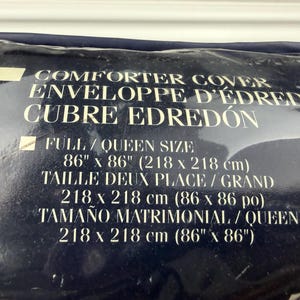 Op de afbeelding: Een marineblauwe dekbedovertrekverpakking. De tekst op de verpakking luidt "COMFORTER COVER" en "FULL/QUEEN SIZE 218 x 218 cm (86 x 86 po)". De verpakking bevat ook vertalingen in het Frans en Spaans.