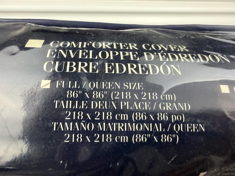 Op de afbeelding: Een marineblauwe dekbedovertrekverpakking. De tekst op de verpakking luidt "COMFORTER COVER" en "FULL/QUEEN SIZE 218 x 218 cm (86 x 86 po)". De verpakking bevat ook vertalingen in het Frans en Spaans.