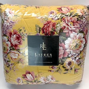 May include: A yellow floral comforter set in plastic packaging. The comforter features a large-scale floral pattern in shades of pink, red, and white. The comforter set is labeled with the brand name "Lauren Ralph Lauren".