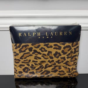 May include: A Ralph Lauren Home bedding item packaged in clear plastic. The fabric features a brown and tan leopard print pattern. The top section of the packaging is a dark blue band with the text RALPH LAUREN HOME printed in gold lettering.
