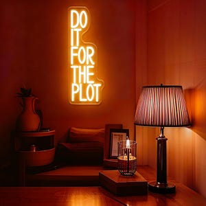 以下が含まれることがあります： 「DO IT FOR THE PLOT」と書かれたネオンサインのある、暖色系の部屋。ストライプのシェードが付いたランプが木製のテーブルの上にあり、ガラスホルダーに入ったキャンドルの隣にあります。花瓶と小さなテーブルも見えます。