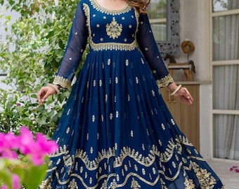 Op de afbeelding: Een lange, vloeiende marineblauwe jurk met ingewikkelde gouden borduursels. De jurk heeft een ronde hals, lange mouwen en een volle rok. De gouden borduursels zijn geconcentreerd rond de halslijn, taille en zoom.