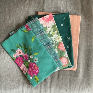 Peut inclure: Un ensemble de cinq carrés de tissu pliés présentant divers motifs et couleurs. La collection comprend un carré sarcelle à motifs floraux roses, un carré sarcelle à lignes pointillées, un carré vert à motifs floraux, un carré vert foncé à formes géométriques blanches et un carré pêche uni.