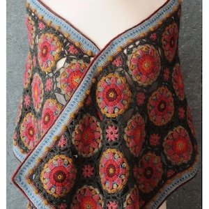 May include: A handmade crochet wrap in a floral pattern. The wrap features a dark gray base with colorful floral motifs in shades of red, pink, and yellow. The edges are trimmed with blue and yellow detailing. The text "SUMMER PALACE WRAP KIT" is at the bottom.