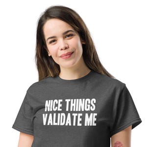 May include: A dark gray t-shirt with white text that reads "NICE THINGS VALIDATE ME".