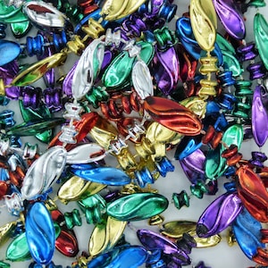 May include: A close-up of a pile of colorful Mardi Gras beads. The beads are in various metallic colors, including gold, silver, green, blue, red, and purple. The beads have an oval shape and are strung together.