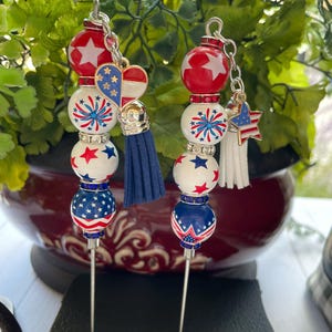 Peut inclure: Deux porte-clés sur le thème patriotique avec des perles rouges, blanches et bleues, des étoiles et des motifs de feux d'artifice. Chaque porte-clés a un pompon, un bleu et un blanc.