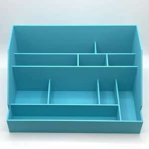 May include: A light blue desk organizer with multiple compartments and shelves. The organizer has a rectangular base and a sloped back, with various sized sections for storage. The color is a solid, bright blue.