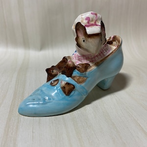 May include: A blue ceramic shoe with three mice inside. The mouse on top is wearing a pink and white hat.
