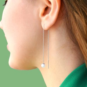 May include: A pair of silver chain earrings with a single pearl dangling from each chain.