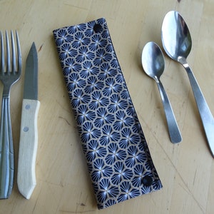 May include: A black and gold patterned fabric cutlery holder with a snap closure. The holder contains a fork, knife, and two spoons.