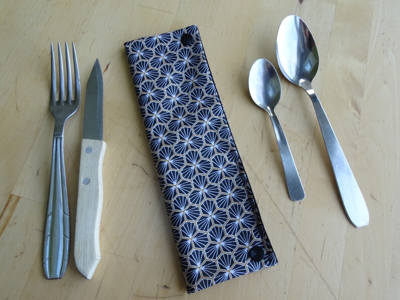 May include: A black and gold patterned fabric cutlery holder with a snap closure. The holder contains a fork, knife, and two spoons.