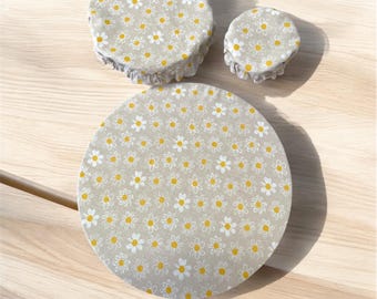 May include: Three beige reusable food covers with a white daisy pattern. The covers are made of fabric and have a ruffled edge.