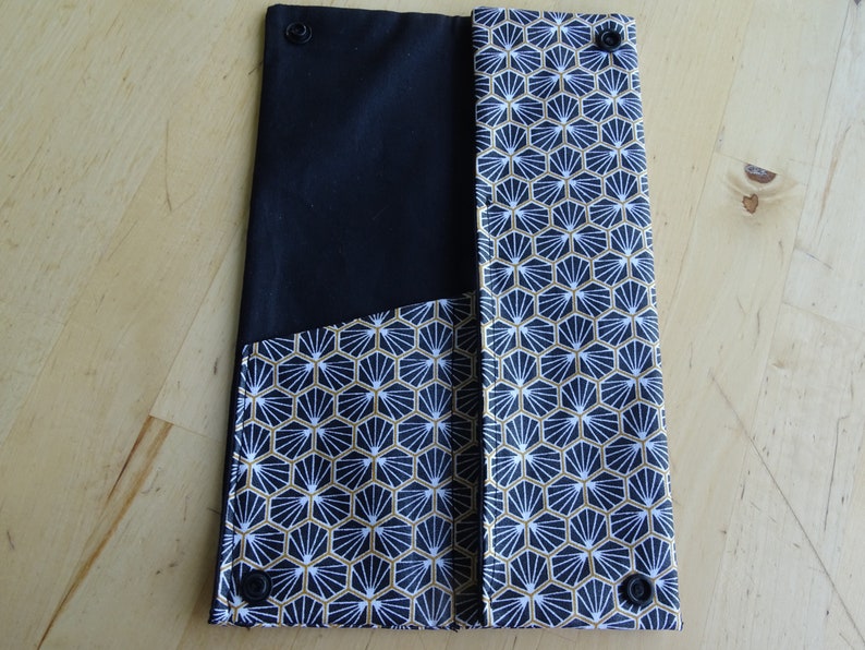 May include: Black and white fabric clutch with a geometric pattern and gold accents. The clutch has two snap closures.