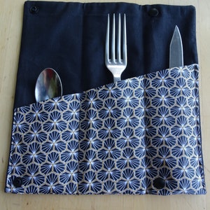 May include: A black fabric cutlery roll with a geometric pattern in white and gold. The roll has three slots for a fork, spoon, and knife.