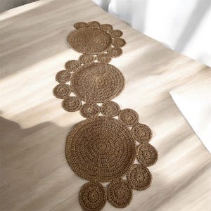 Peut inclure: Un chemin de table en crochet marron avec un motif de cercles qui se chevauchent. Le chemin de table est fait de fibres naturelles et a un style rustique et bohème.