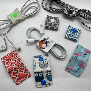 Könnte beinhalten: Sortiment an bunten Stoff-Kabelorganisatoren mit verschiedenen Mustern und Knopfverschlüssen. Die Organisatoren sind so konzipiert, dass sie Kabel und Drähte ordentlich und organisiert halten.