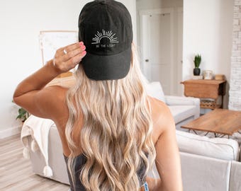 May include: A black baseball cap with a white sun and the text "BE THE LIGHT" embroidered on the front.