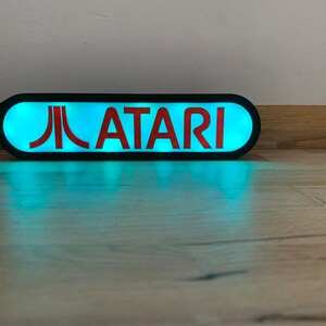May include: A black and red illuminated sign with the text "ATARI" and the Atari logo. The sign is lit with a bright blue light.