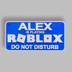 May include: Blue sign with white text that reads "Alex is playing Roblox. Do not disturb."