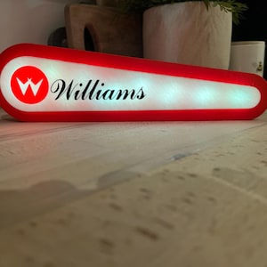 May include: An illuminated sign with the text "Williams" and a double "W" logo in a red circle. The sign is red and white.