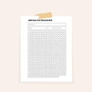 May include: A white 365 Days Tracker sheet with a grid of numbers for daily habit tracking. The title "365 DAYS TRACKER" is at the top, with spaces for the starting date and habit. The sheet is held in place with a piece of tan tape.