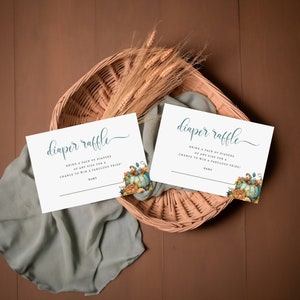 May include: Two white cards with the text "diaper raffle" in teal calligraphy. The cards have a fall-themed design with pumpkins, leaves, and flowers. The text on the cards reads "Bring a pack of diapers of any size for a chance to win a fabulous prize!"