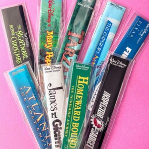 May include: A collection of Disney VHS tape bookmarks, each encased in clear plastic. Titles include "The Nightmare Before Christmas," "Mary Poppins," "Tarzan," "The Emperor's New Groove," "Atlantis," "James and the Giant Peach," "Homeward Bound," and "Inspector Gadget."