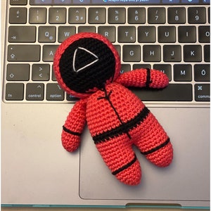 May include: A crocheted red and black doll with a triangular face. The doll is lying on a silver laptop keyboard.