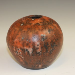 May include: A small, round ceramic vase with a mottled brown, orange, and white glaze. The vase has a small opening at the top.