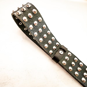 May include: Black leather belt with rows of silver-colored, rounded studs. The belt has a buckle and several eyelets for adjustment. The design is edgy and rock-inspired.
