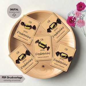 May include: A wooden tray holds five cards with a candy and the text "EIN GROBES Dankeschön!" in black. The candy is wrapped in black and yellow paper. The words "DIGITAL DOWNLOAD" are in a circle in the upper left corner. Pink flowers are in the upper right.