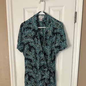 Puede incluir: Un vestido largo de color azul oscuro con un estampado de hojas verdes y blancas. El vestido tiene mangas cortas y un escote en V. La etiqueta de la marca dice "Papillon".