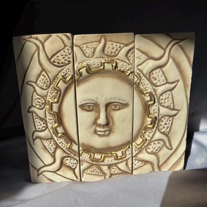 May include: A three-piece ceramic wall art sculpture depicting a stylized sun with a human face. The sun is surrounded by rays and has a gold-colored border.