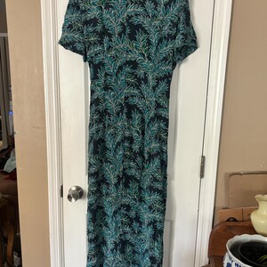 Puede incluir: Un vestido largo de color azul oscuro con un estampado de hojas verdes y blancas. El vestido tiene mangas cortas y cuello.