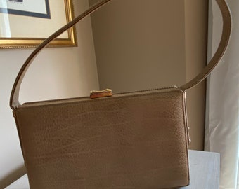 May include: A beige leather handbag with a gold clasp and a long strap. The bag has a textured surface and a rectangular shape.
